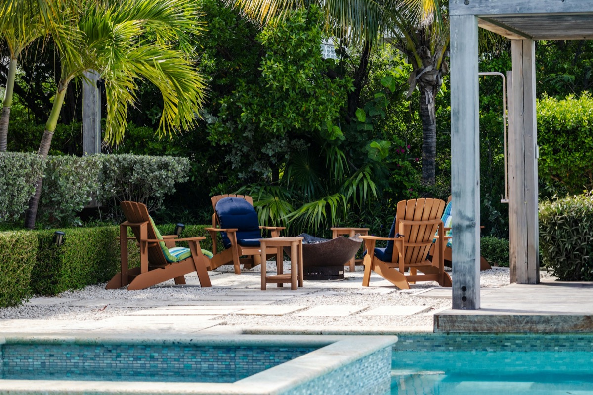 Timber chairs around a fire pit beside a pool in a tropical garden