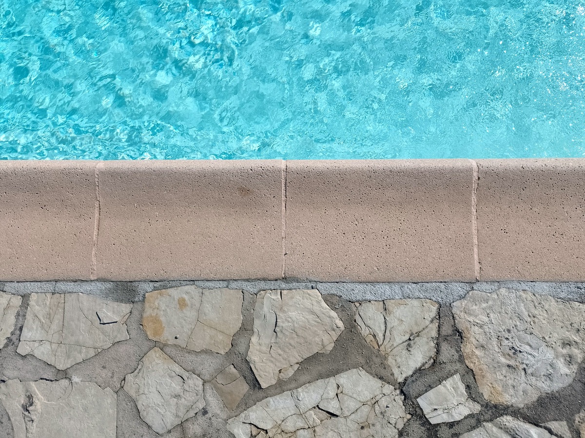 Clear pool water meeting a sandstone coping and a natural stone wall
